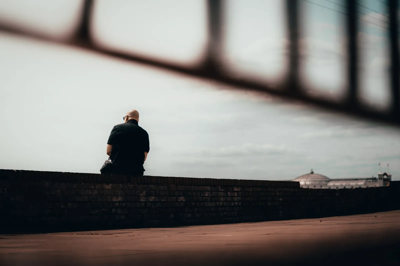 A solitary man sits contemplatively on a wall in Brighton and Hove, England.