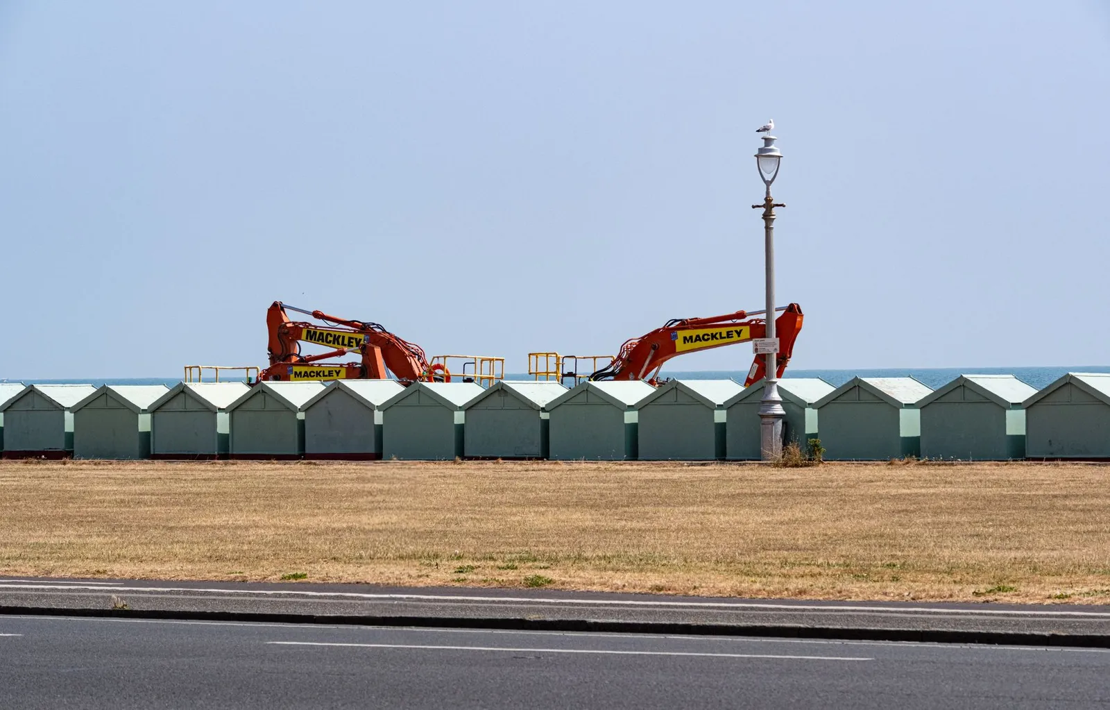 A row of beach huts with construction equipment along Brighton and Hove's coastline.