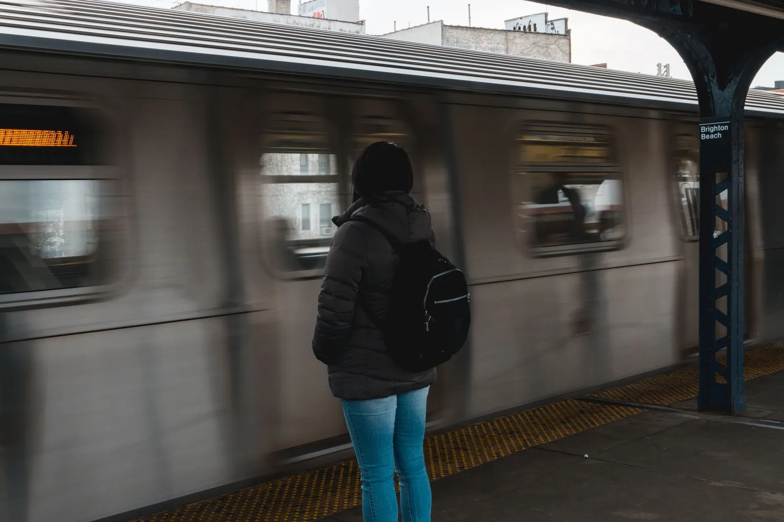 A person in winter clothing waiting for a train at Brighton Beach subway station.