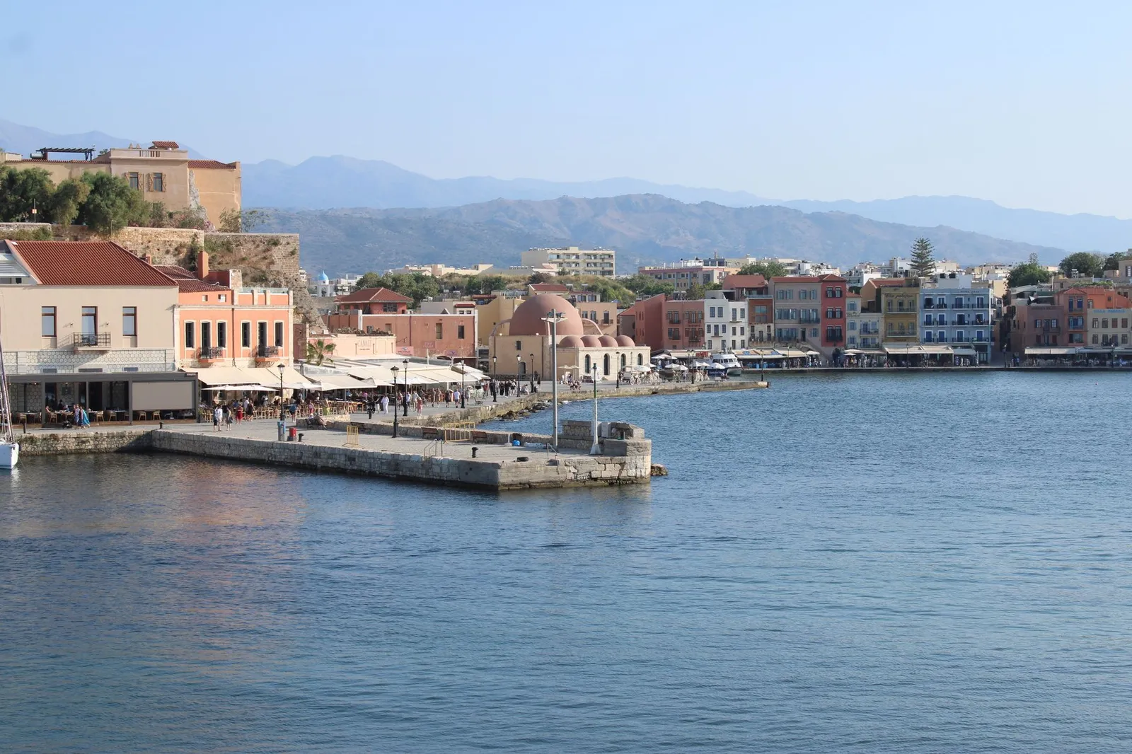 Scenic view of Chania harbor featuring traditional buildings and mountains in Greece.