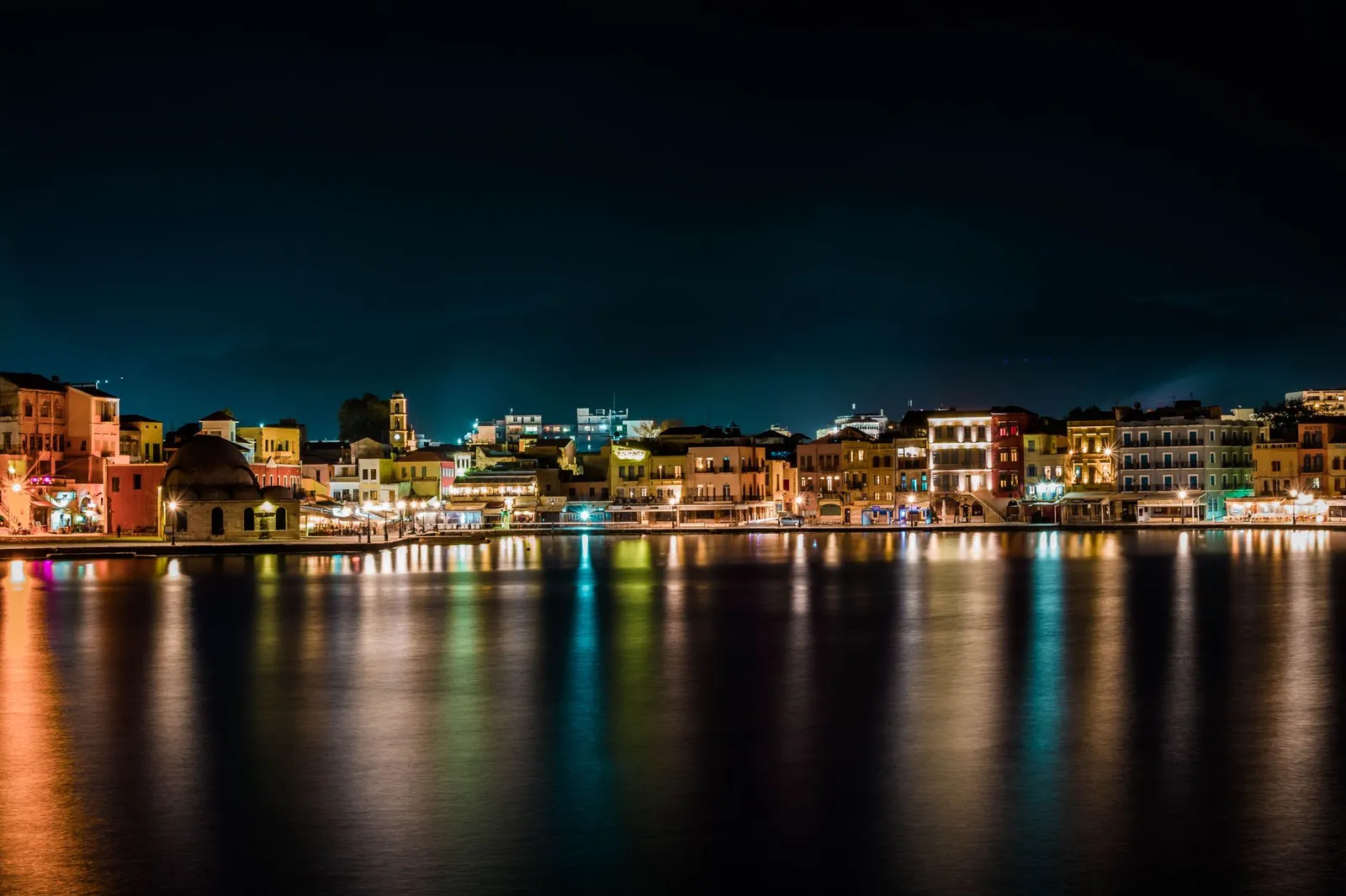 Charming waterfront cityscape of Chania, Greece, illuminated at night with reflections in the water.