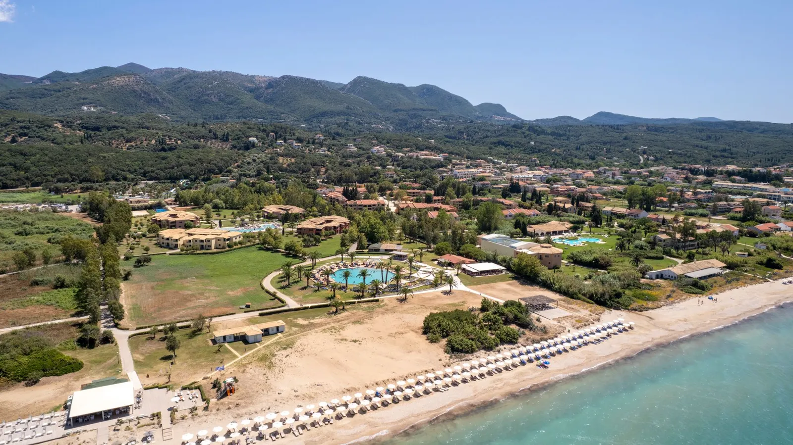 Stunning aerial view of a beachfront resort in Corfu, Greece, showcasing sandy beaches and lush greenery.