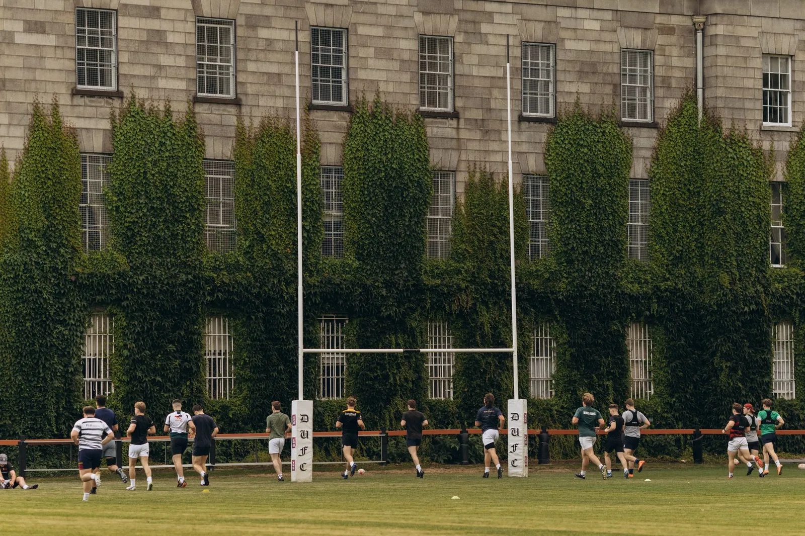 Rugby players practice on lush grounds of Trinity College Dublin.