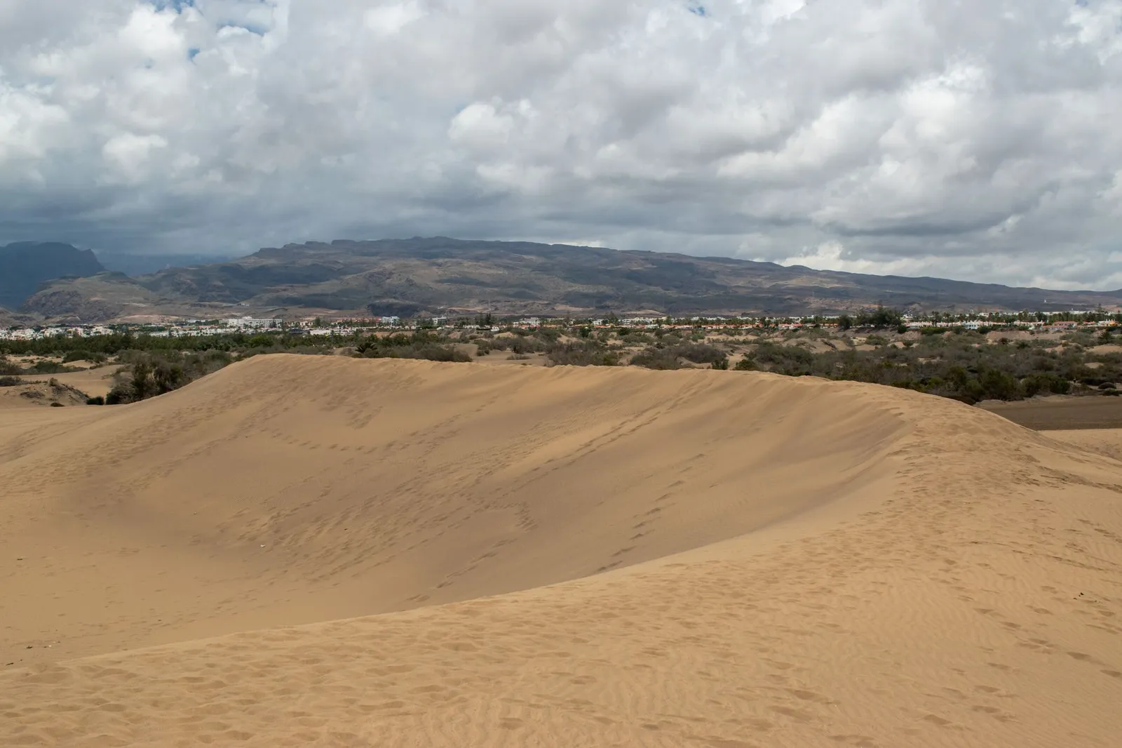 Scenic view of Maspalomas sand dunes with a mountainous backdrop in Gran Canaria.