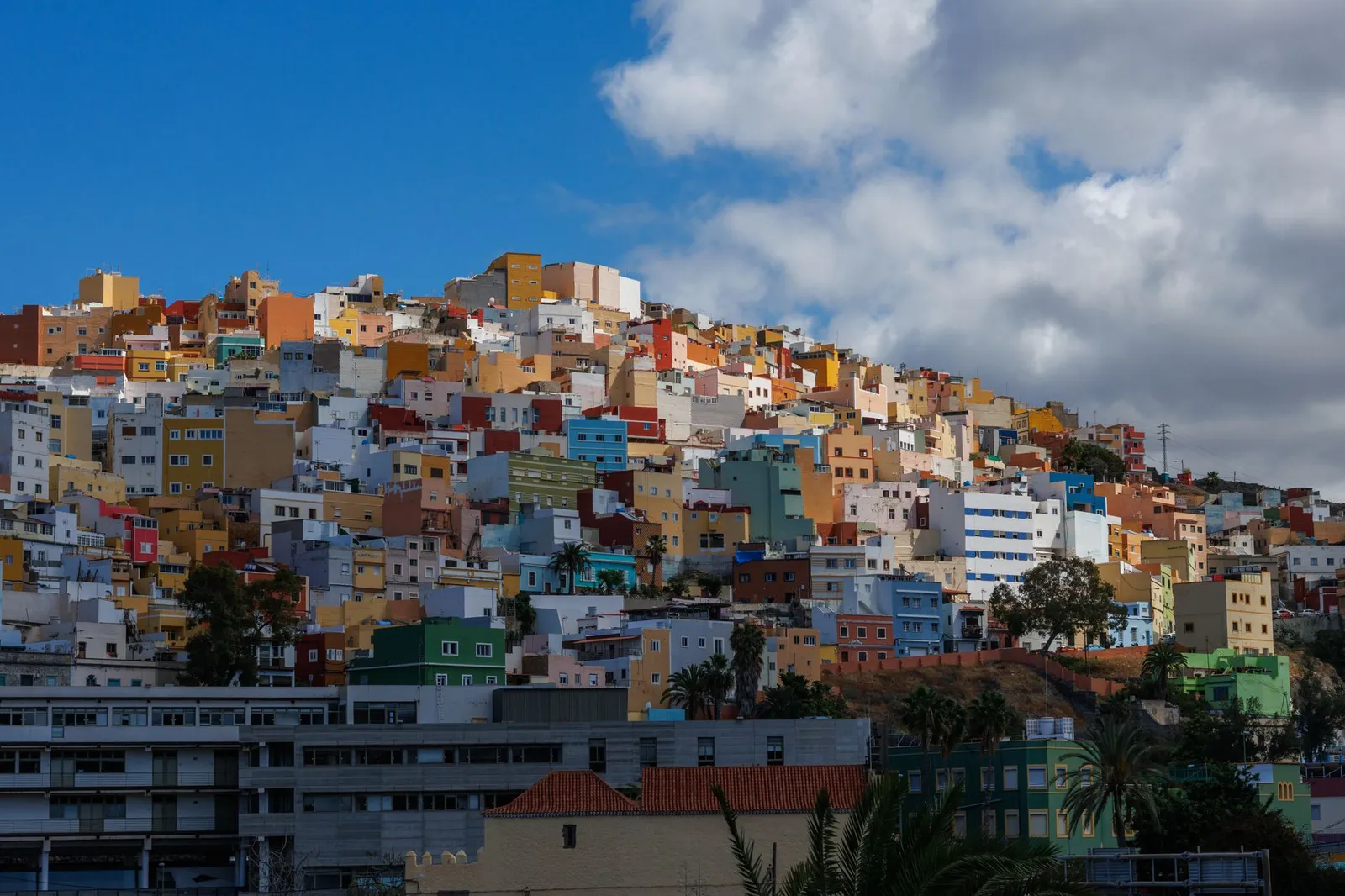 A vibrant cluster of colorful hillside buildings under a bright blue sky in Las Palmas de Gran Canaria, Spain.