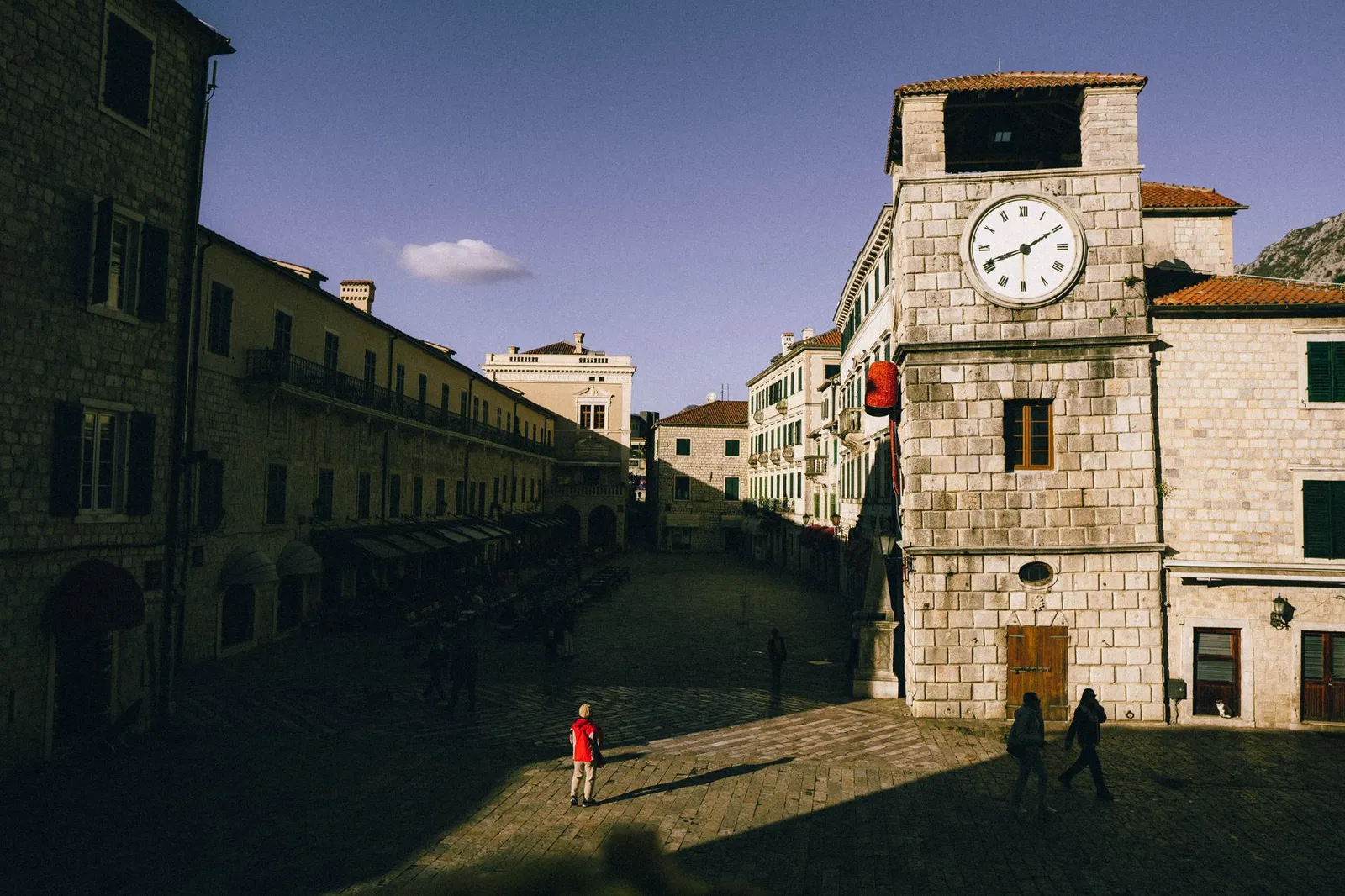 Sunlit clock tower and medieval architecture at Kotor's Old Town square.