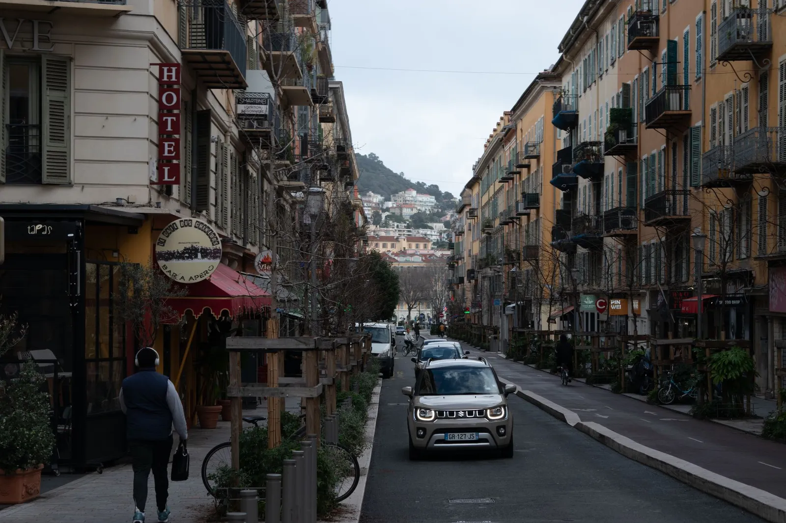 Quaint street view in Nice, France with buildings, cars, and pedestrians.