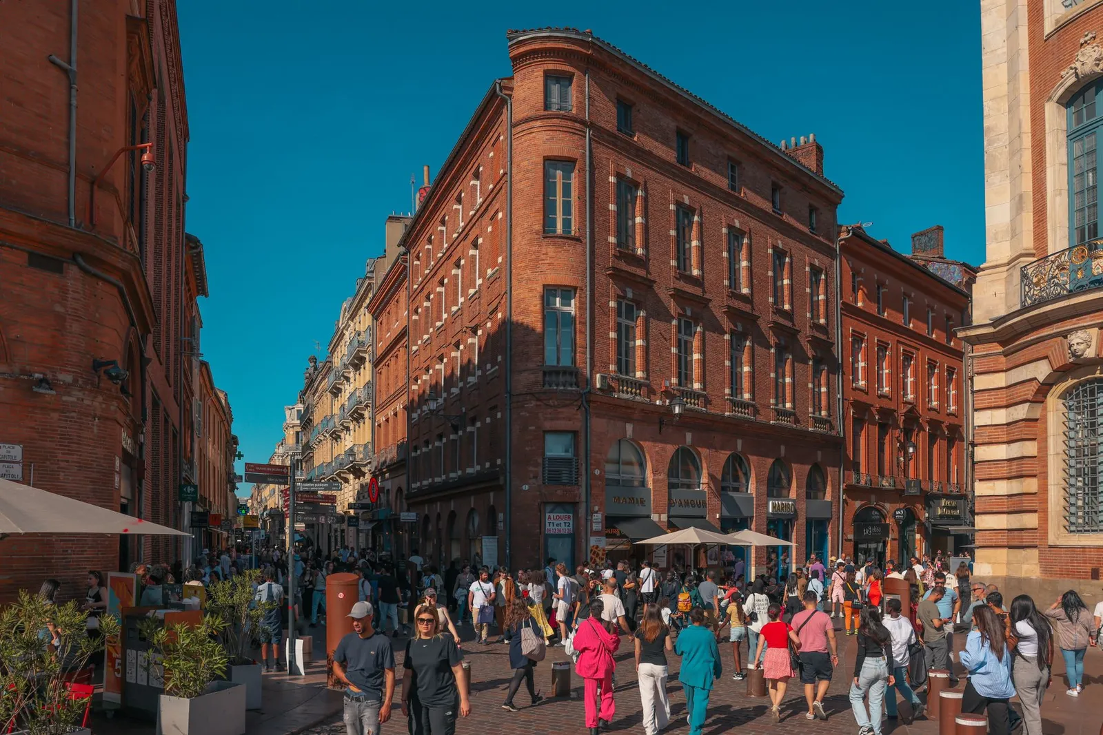 Vibrant street scene in Toulouse's historic district with crowds and red brick architecture.