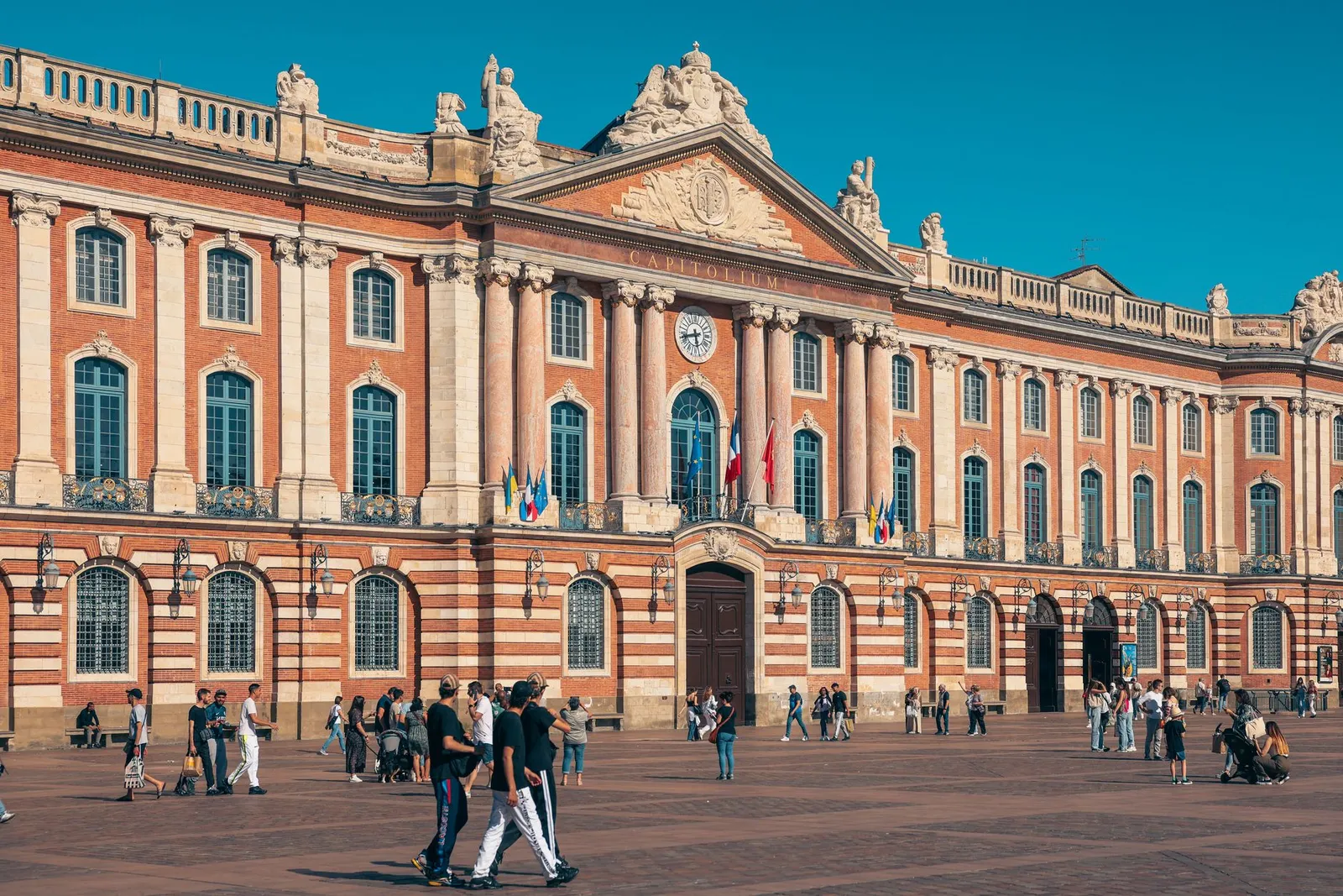 The iconic Capitole de Toulouse with people enjoying the sunny plaza in France.