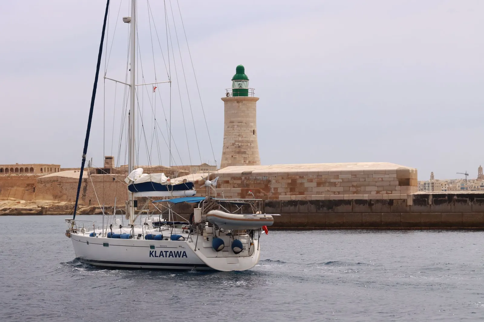 A sailboat named Klatawa sails past a historic lighthouse in Valletta, Malta.