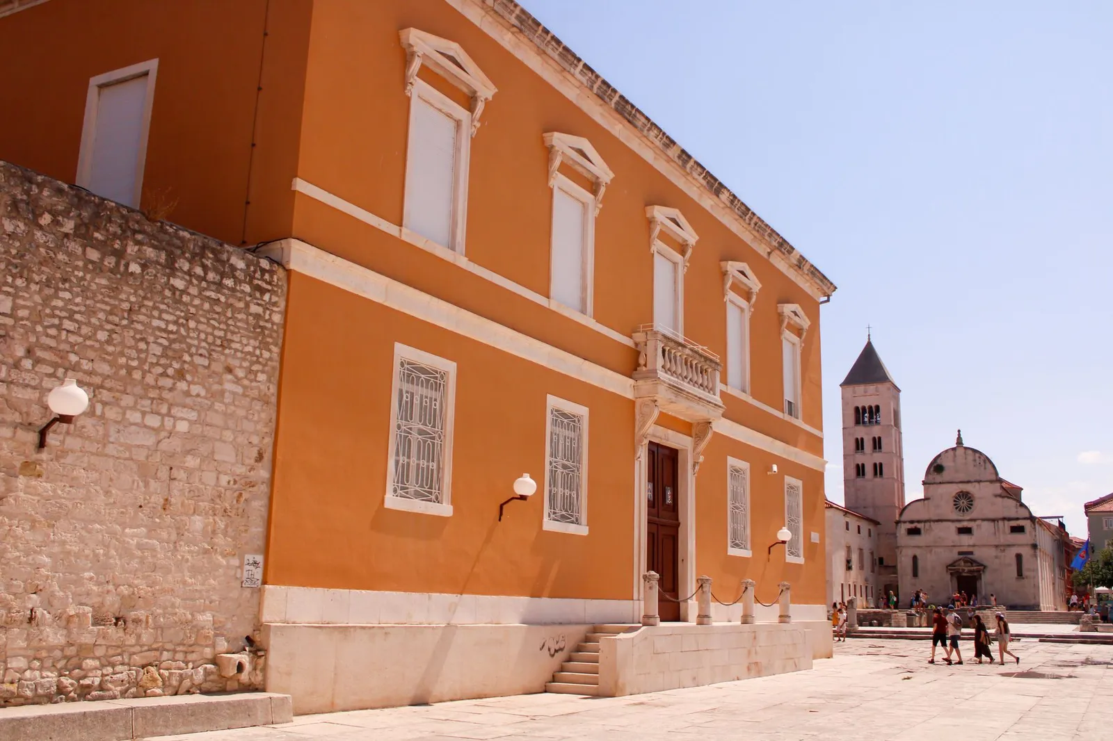 Explore the charming orange facade of a historic building in Zadar with a tower in the background.